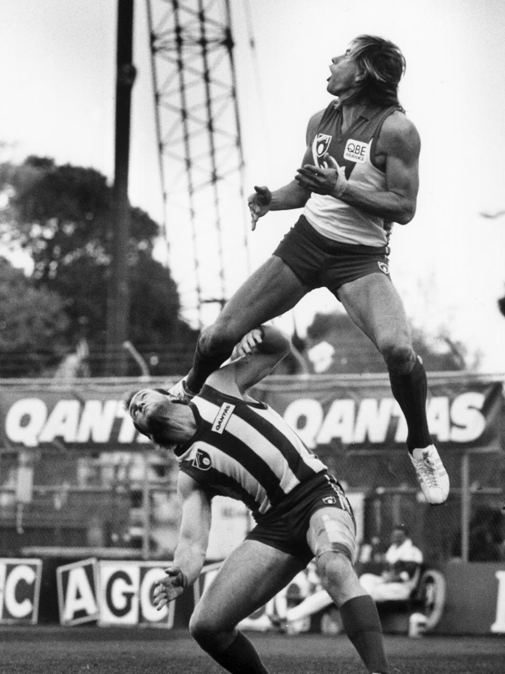 25/04/1991. Warwick Capper flies over Michael Martyn (Mick Martyn). North Melbourne (Kangaroos) v Sydney Swans. Anzac Day. MCG during the Southern Stand redevelopment. Picture: BRUCE HOWARD. Neg: 910426/1-24 (21?)